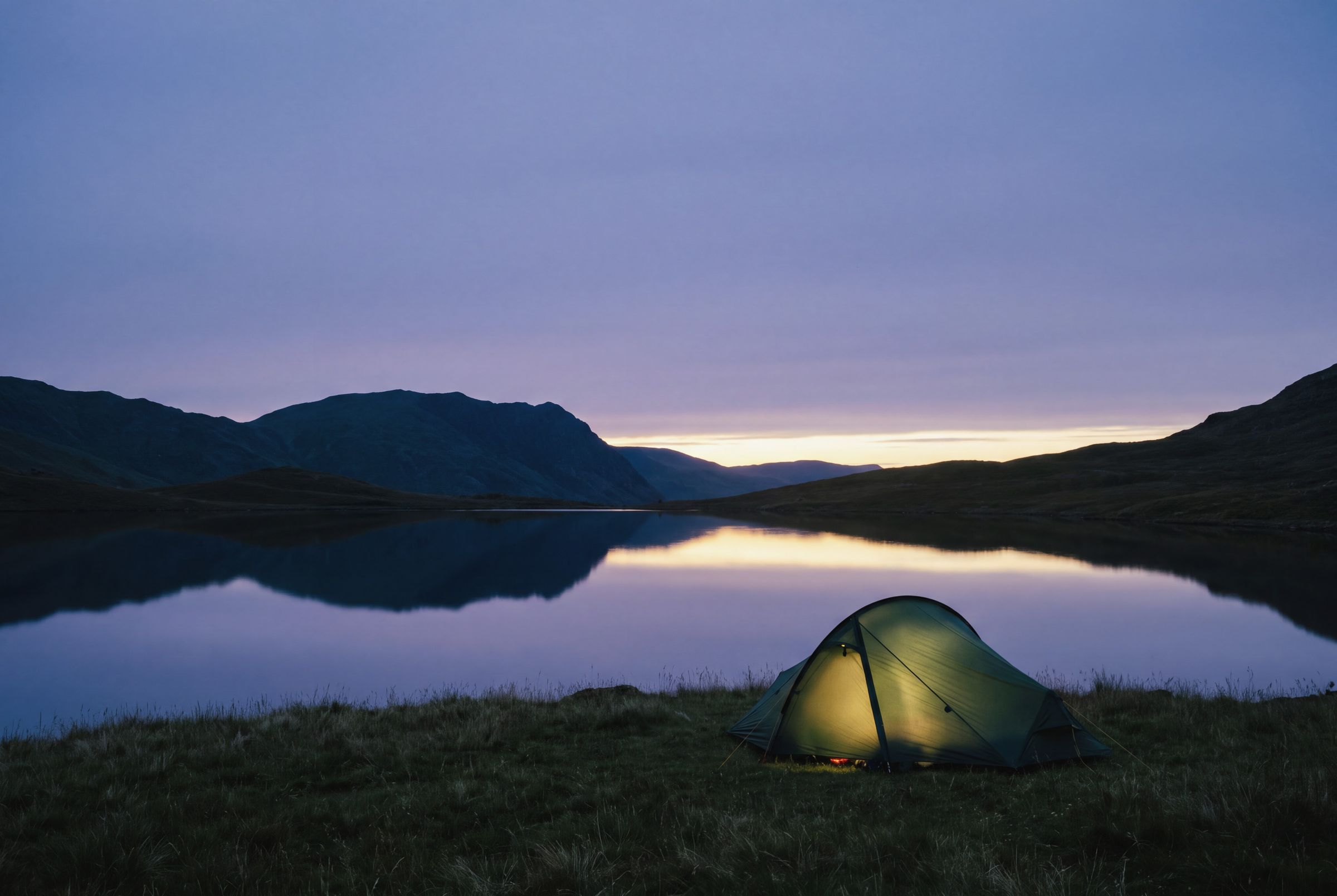 A lit tent beside a Lake District tarn at dusk